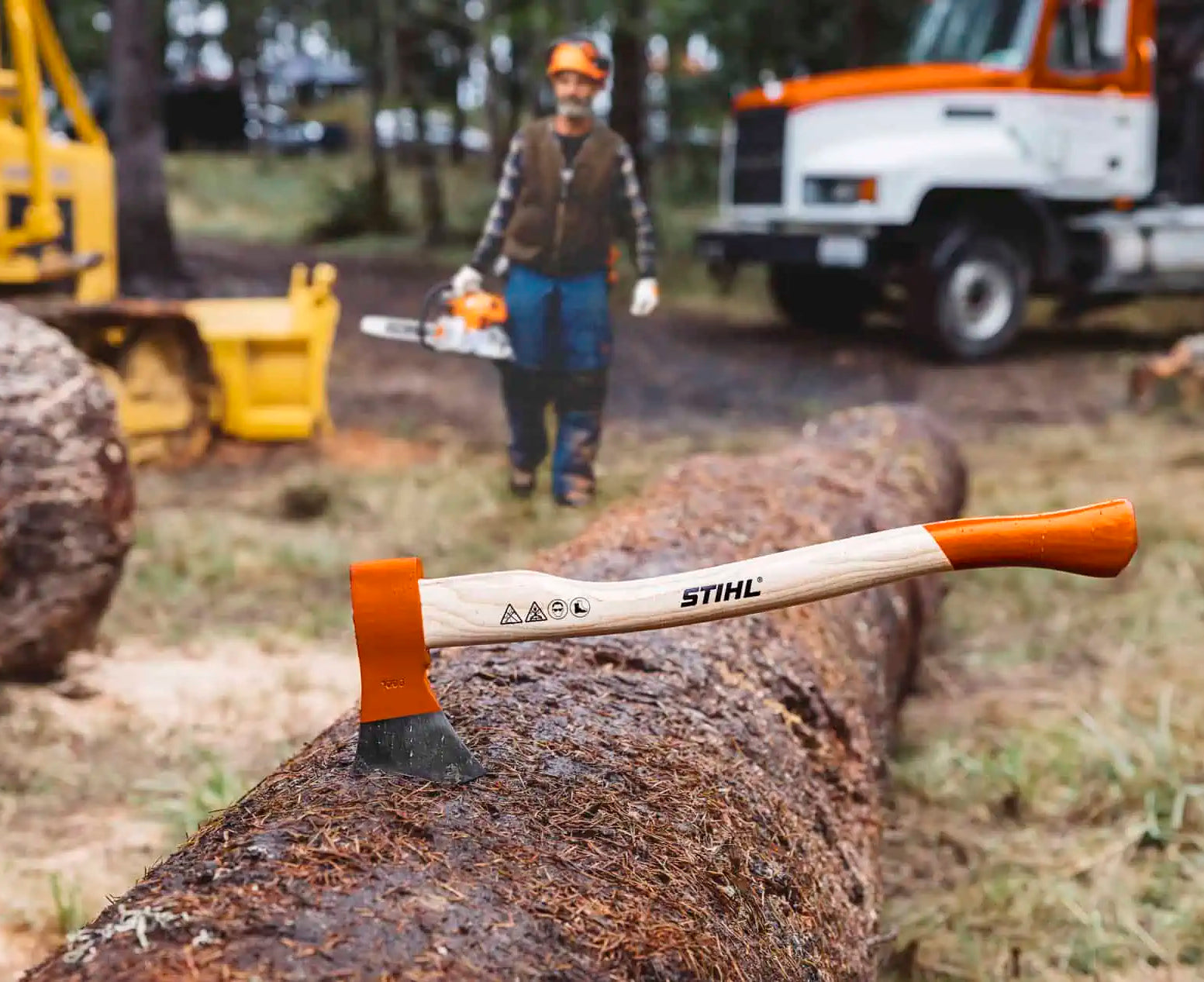 STIHL axe on a log with a person and equipment in the background