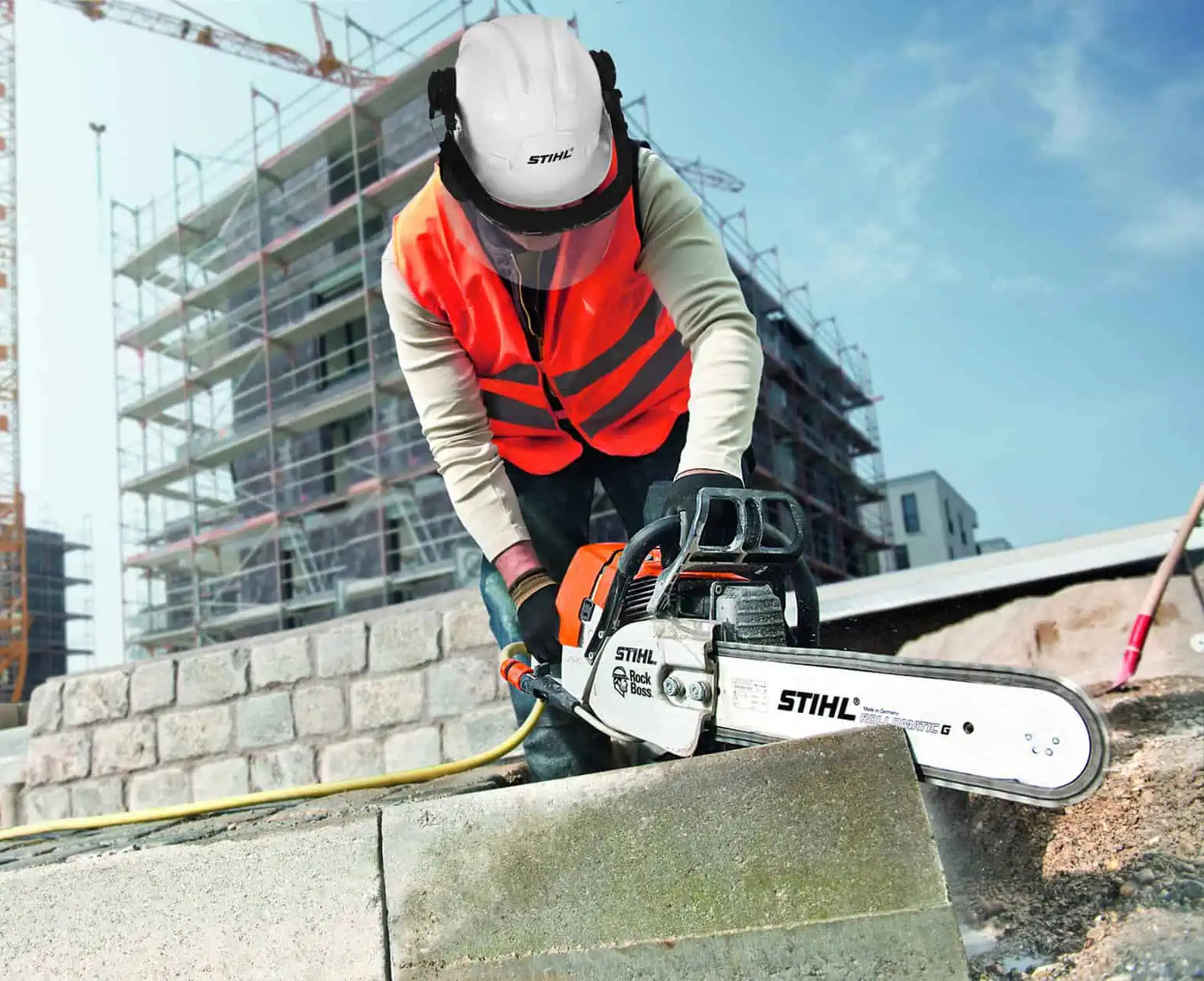 Person using a chainsaw on a construction site with buildings in the background