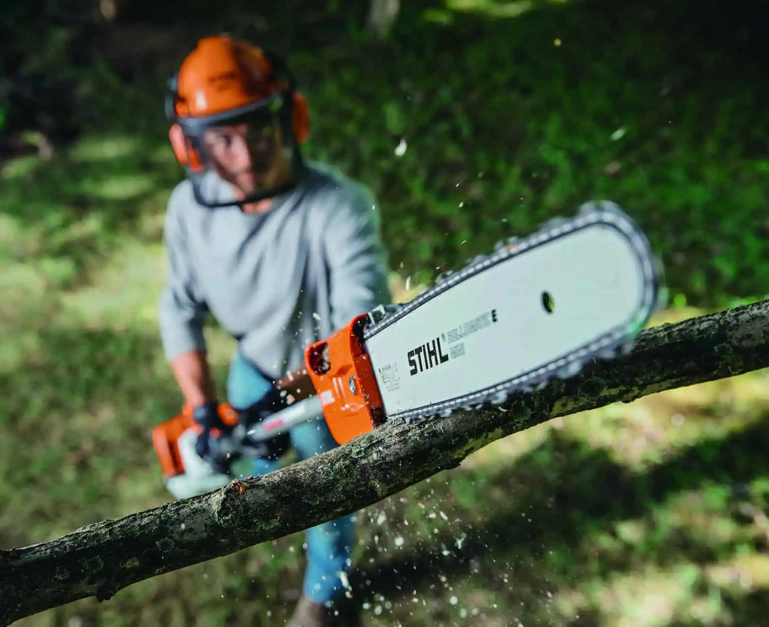 Person using a Stihl chainsaw to cut a branch outdoors.