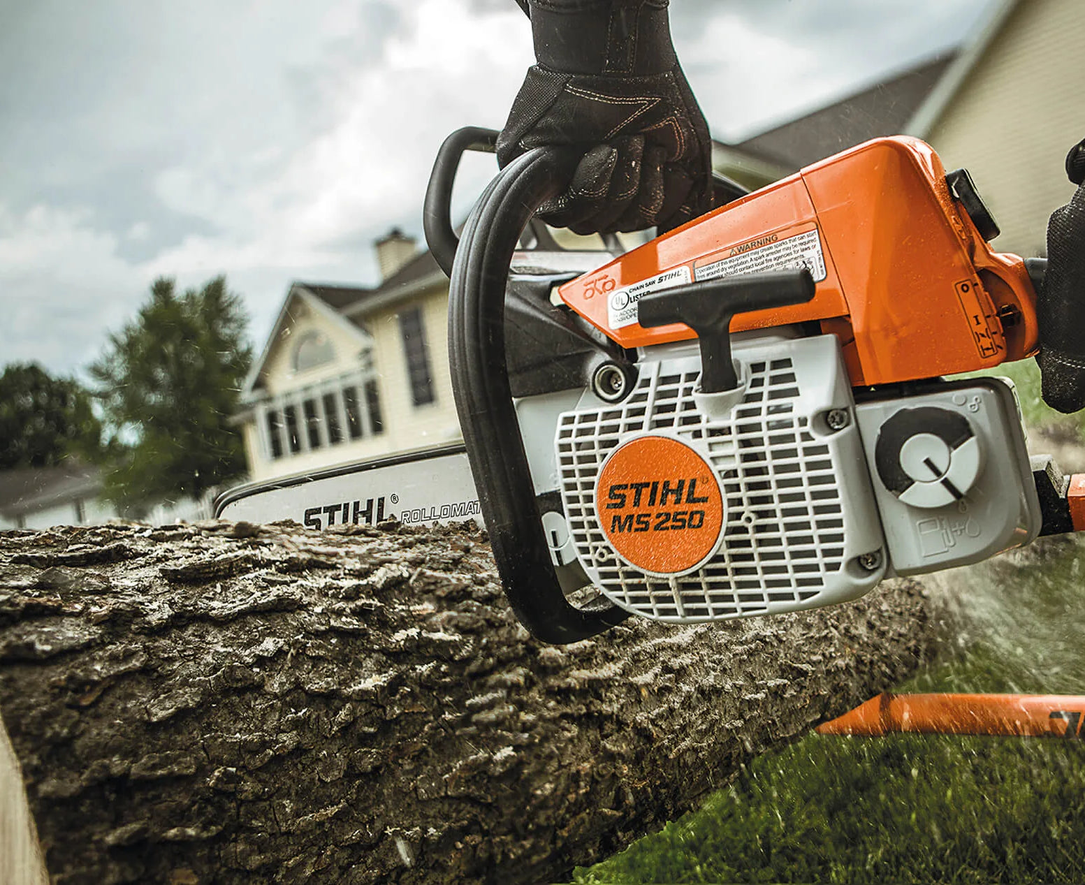 Stihl chainsaw cutting a log with a house in the background