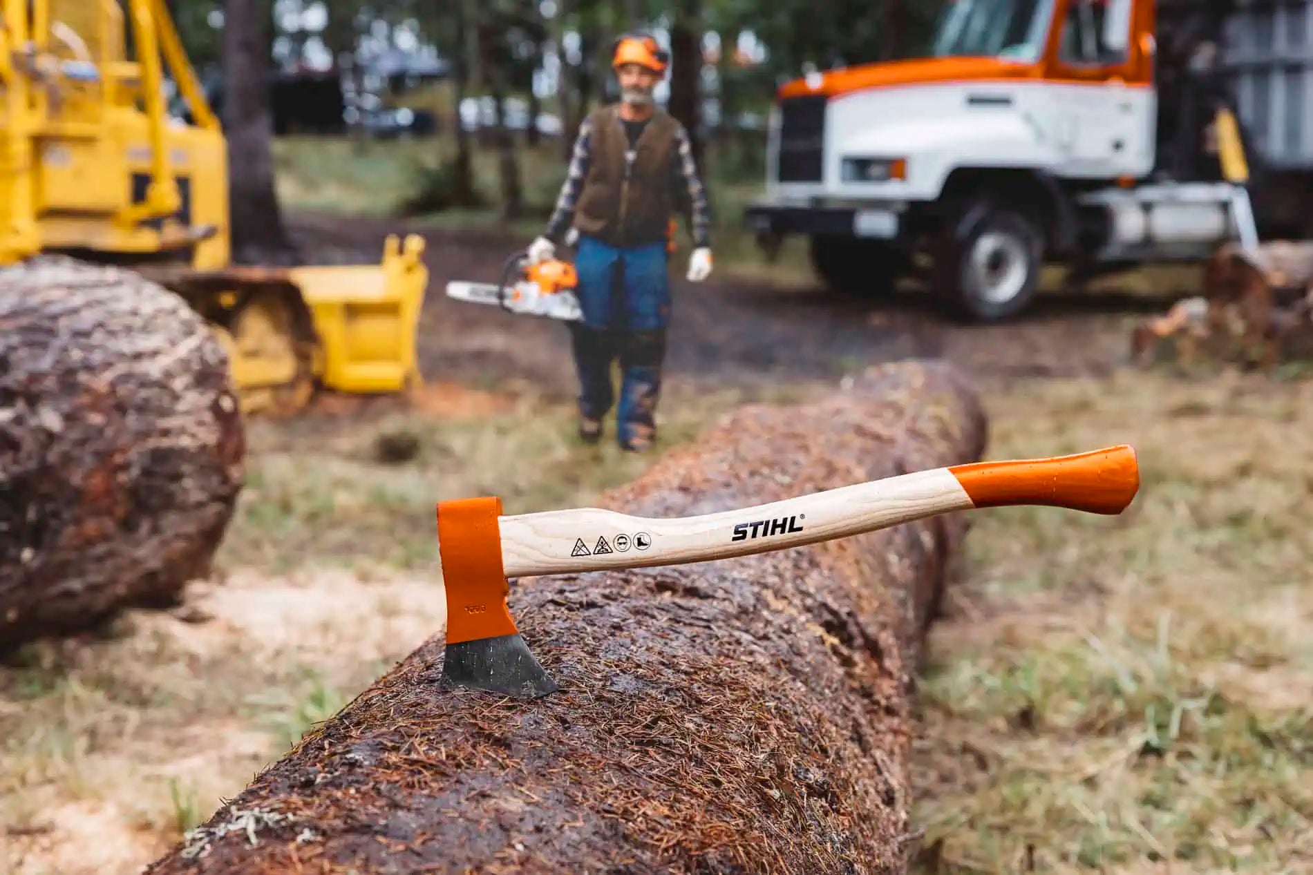 STIHL axe on a log with a person and equipment in the background