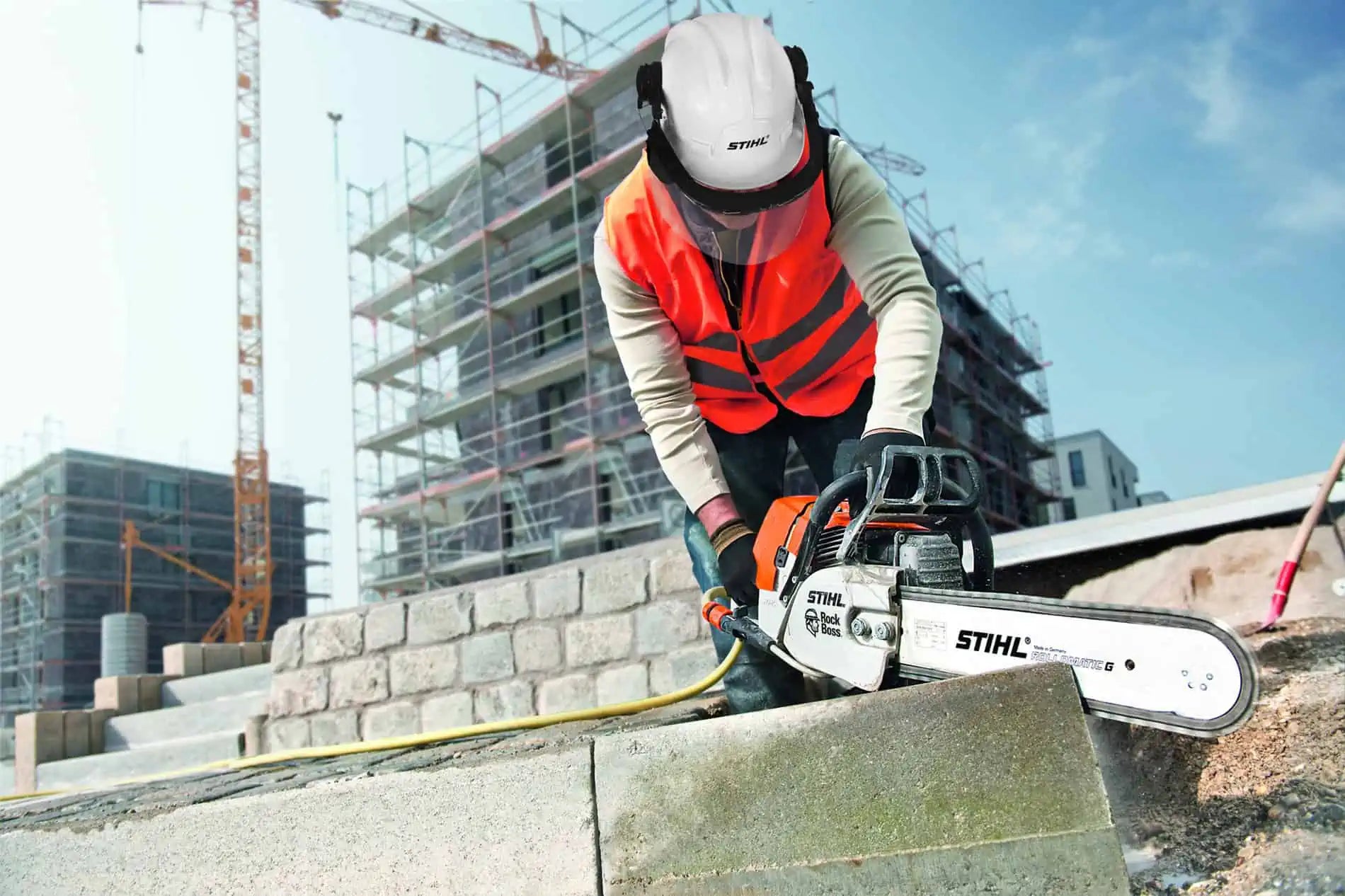 Person using a chainsaw on a construction site with buildings in the background