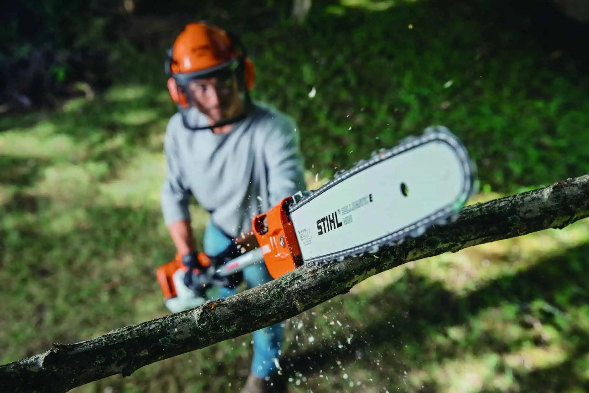 Person using a Stihl chainsaw to cut a branch outdoors.