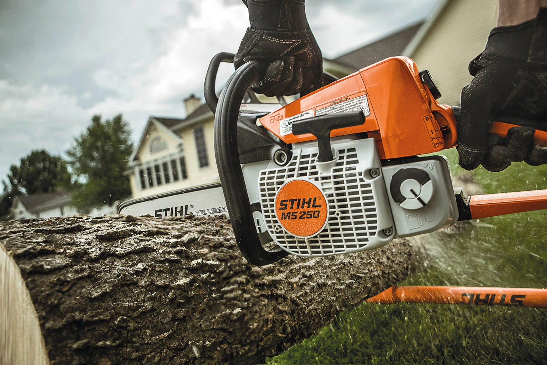 Stihl chainsaw cutting a log with a house in the background