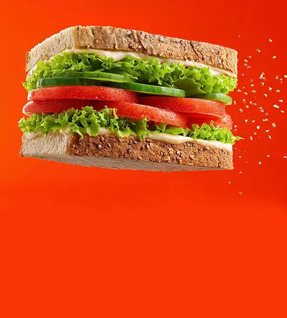 Half-cut sandwich with lettuce, tomato, and cucumber on a red background